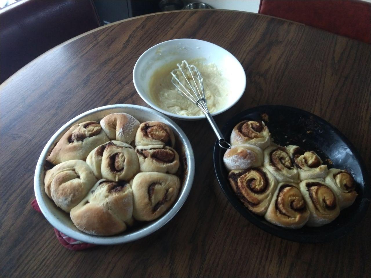 Cinnamon rolls in pie tins next to a bowl of frosting.