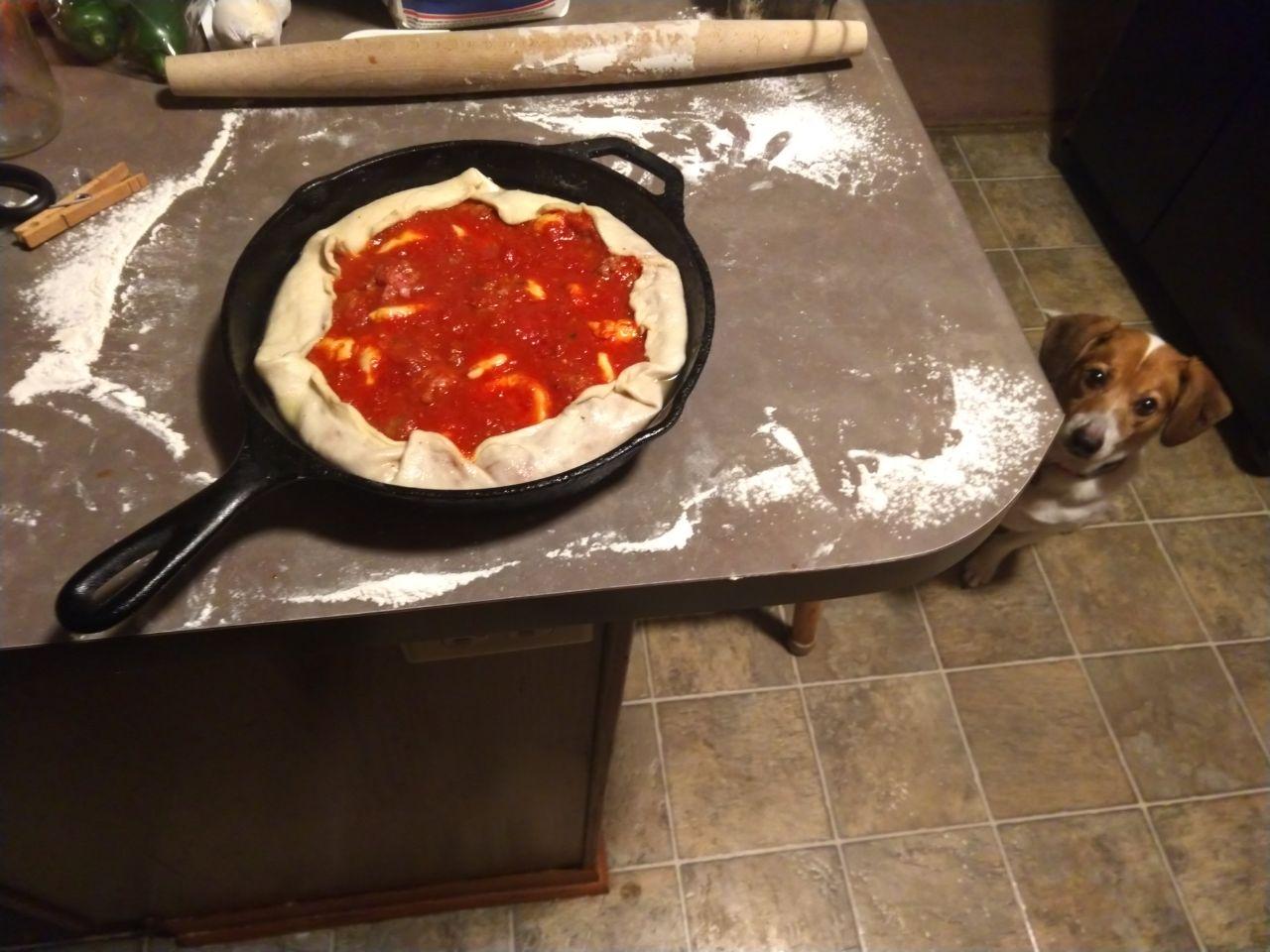 Deep dish pizza after filling with cheese, sausage, and sauce.