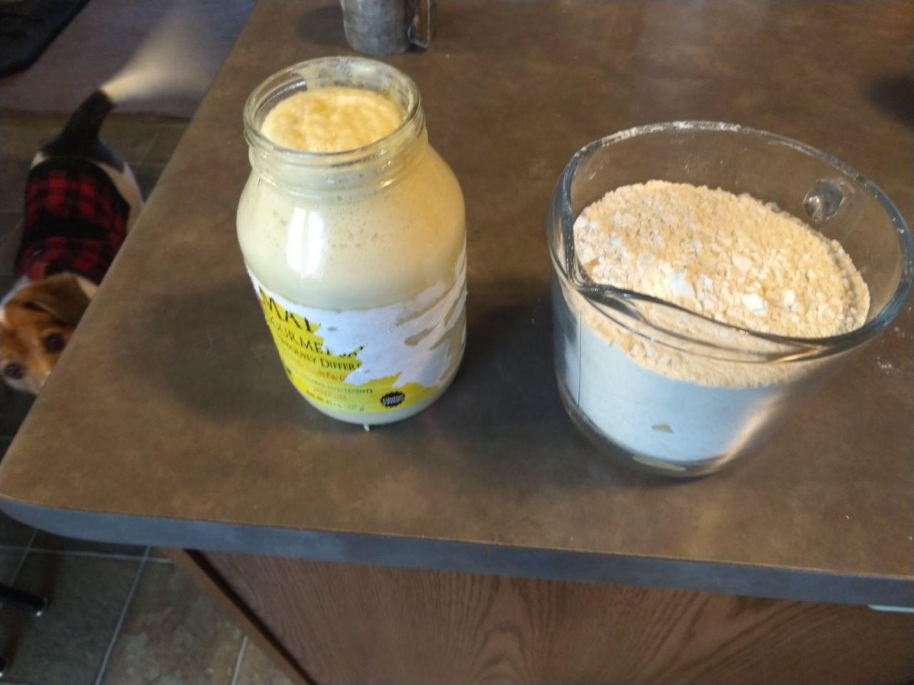 Dough starter mixed in a jar next to a measuring cup of flour.