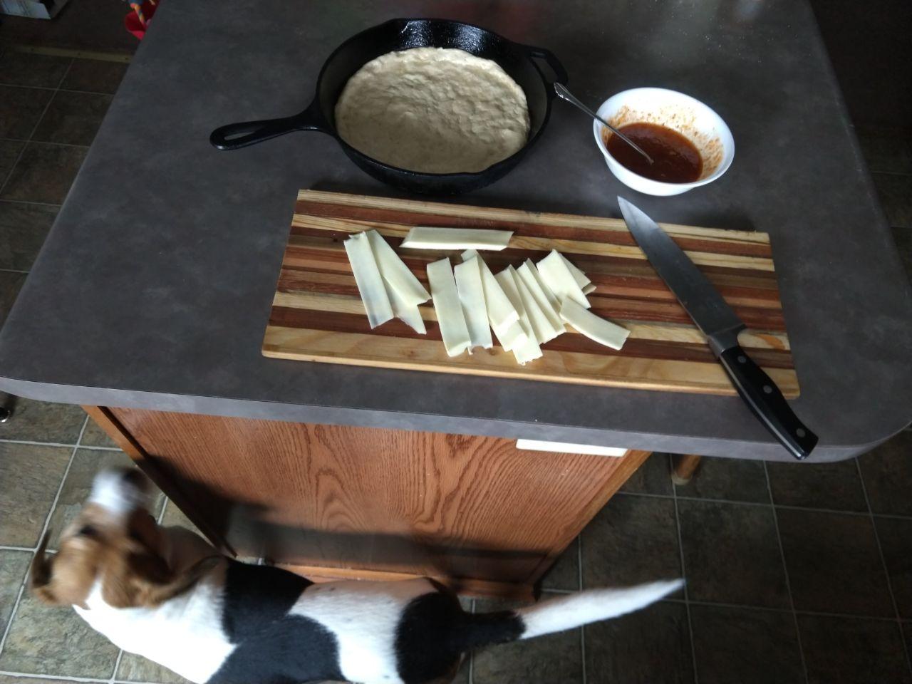 Cutting cheese to place on the pizza, with the mixed sauce and dough rising in the pan.