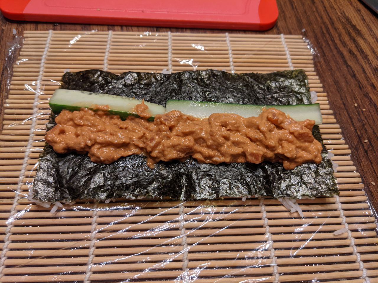 Rolling spicy tuna roll on bamboo mat.