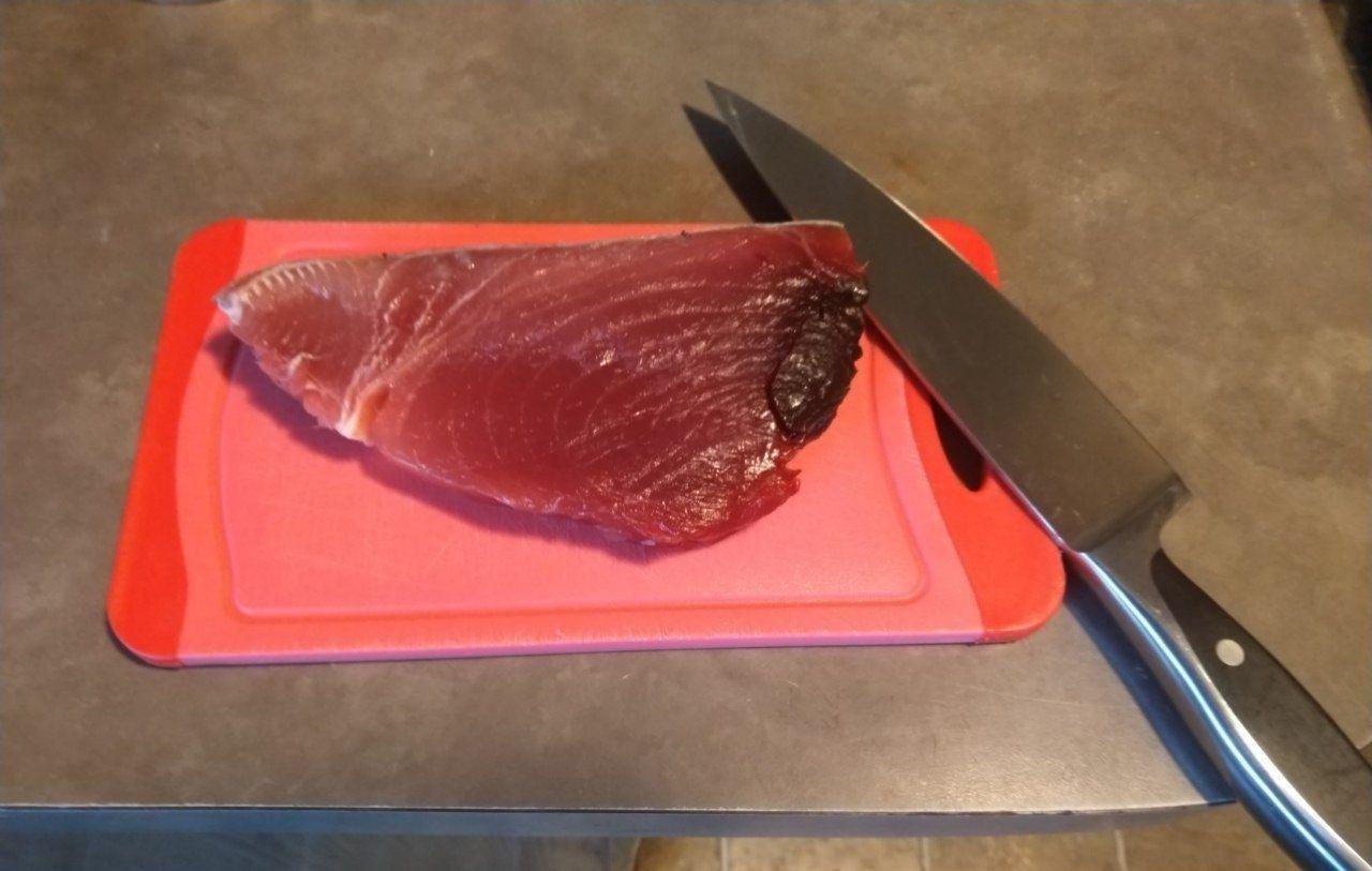 Raw tuna steak on a cutting board with a knife.