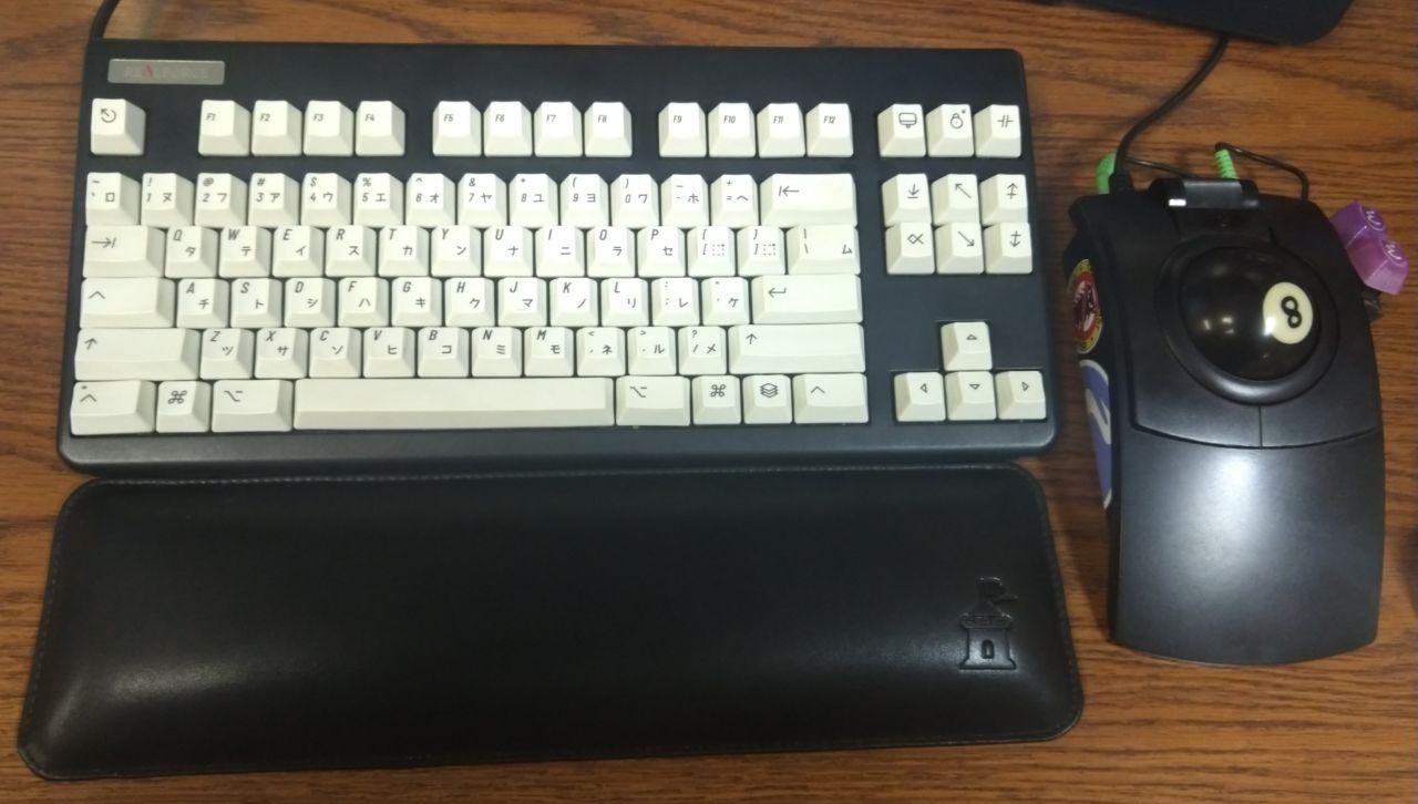 Black RealForce keyboard with white keycaps, next to a black CST trackball with a pool ball.